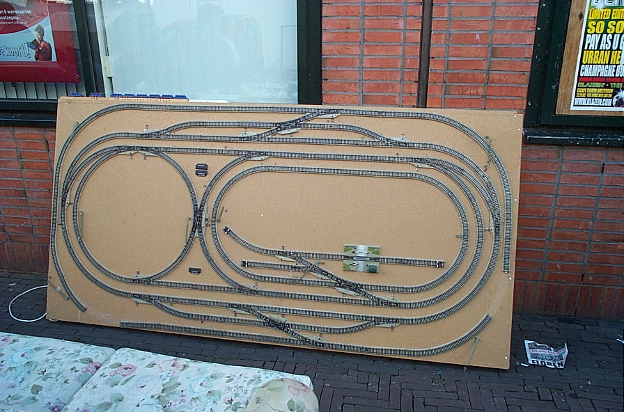 Track plan test-laid on a particleboard sheet, with an oval, turnouts and sidings, the board standing against a wall, no scenery