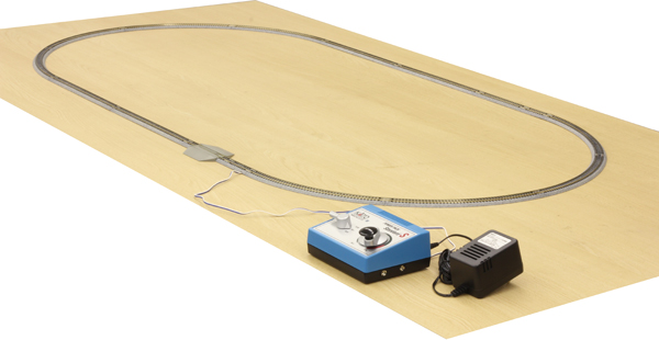A KATO Unitrack oval on a wooden board, with a blue power pack, an AC adapter and a section of feeder track with a wire beside it