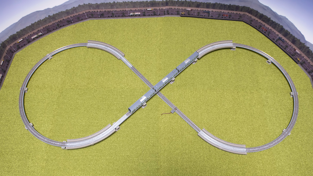 A TOMIX grade-separated figure-8 layout on a green flocked board, with a train on the bridge, seen from above