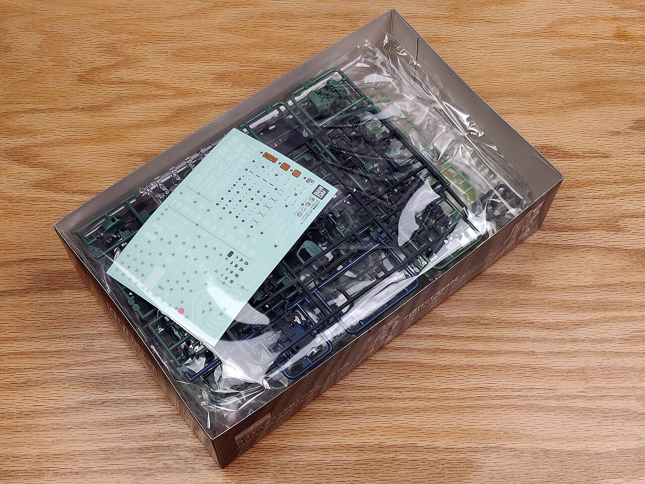 An opened box of an unassembled kit: green and dark blue sprues in a plastic bag, with a decal sheet on top