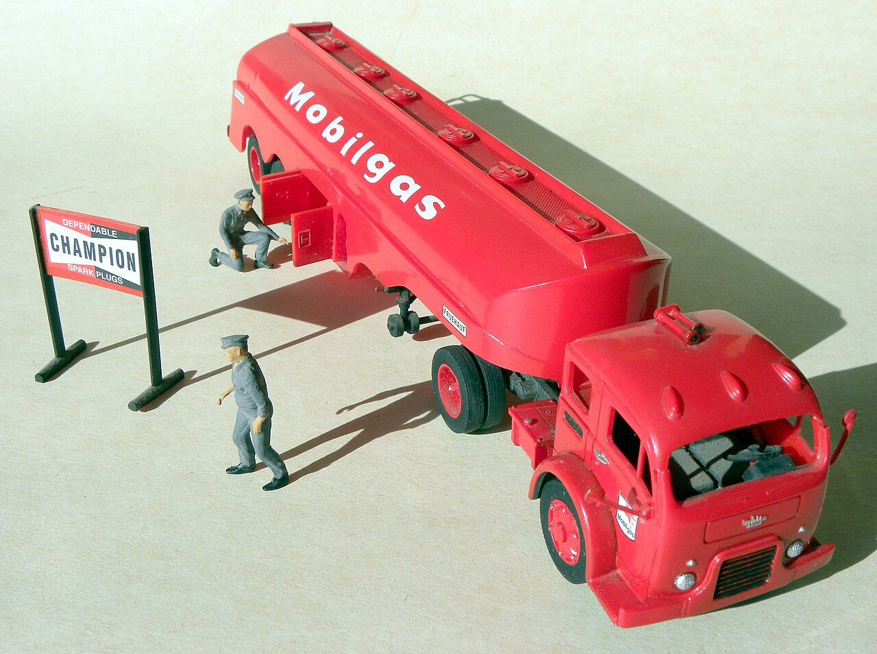 A red Mobilgas tanker truck model with two gas station attendant figures and a Champion spark plug sign