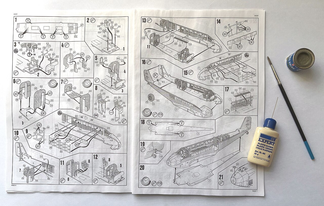 An open Revell instruction sheet next to a bottle of plastic cement, a pot of paint and a brush