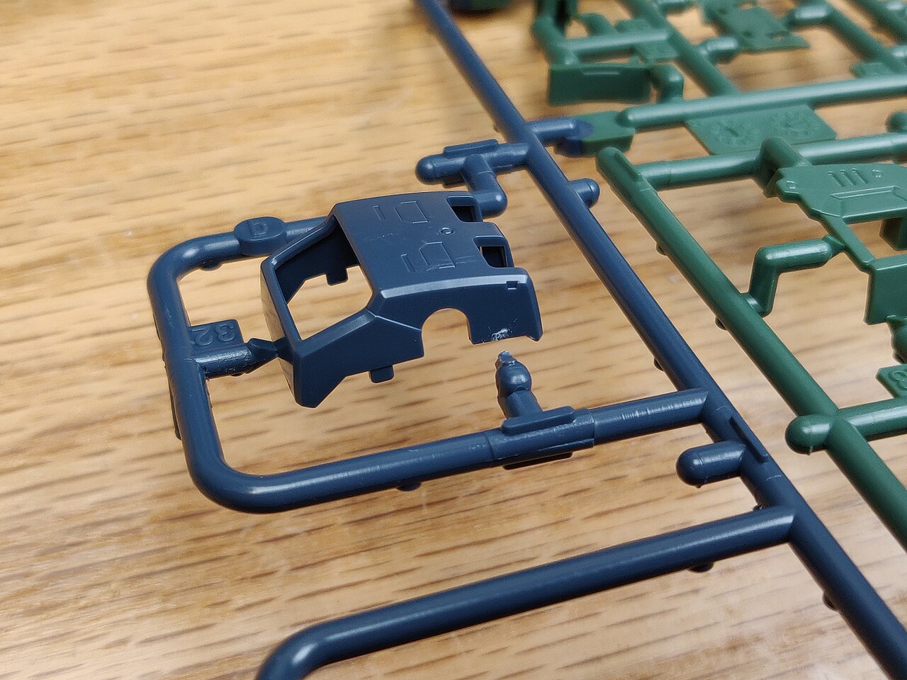 A dark blue sprue with a small gate nub left beside a removed part, with part numbers molded into the sprue